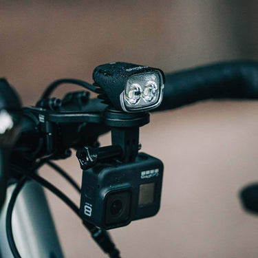 Magicshine MJ-906S front bike light mounted on handlebars with attached action camera, water droplets visible on light.