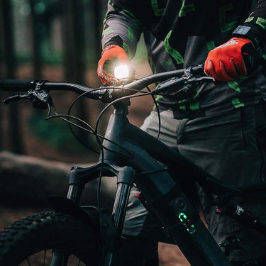 Cyclist adjusting Magicshine MJ-906S front bike light on mountain bike handlebars in forest